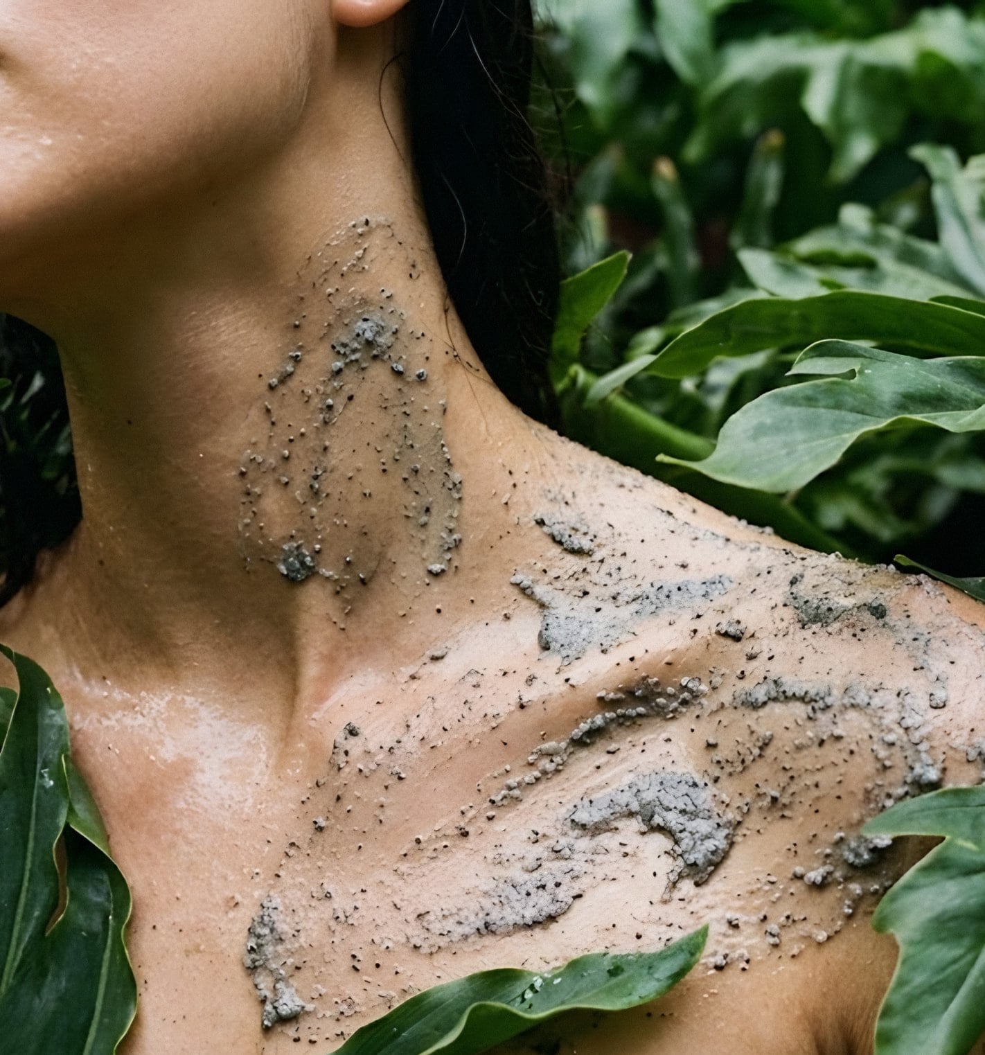 Mineral clay drying on a woman's neck and collarbone among broad green leaves