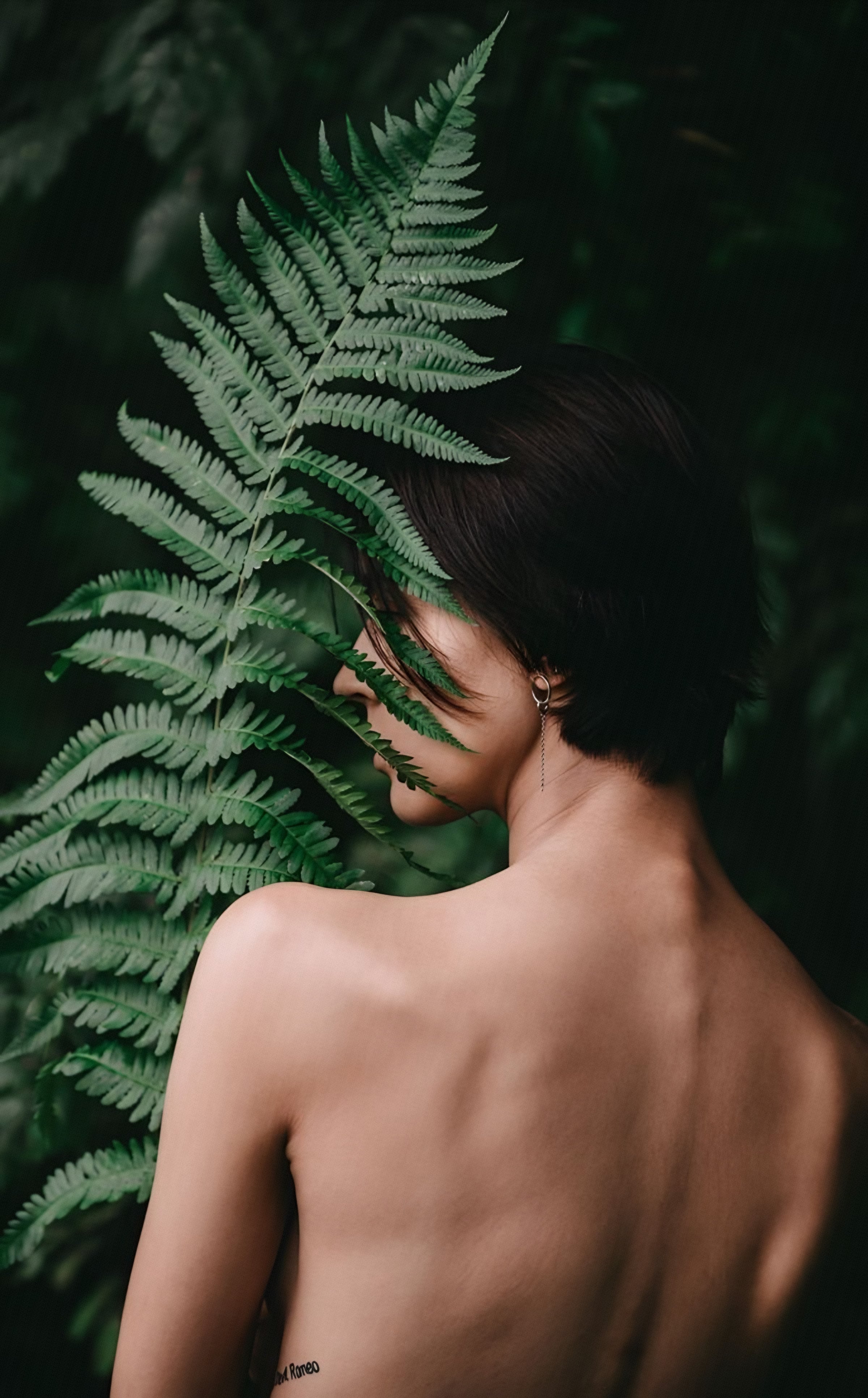 A bare shoulder turned toward a large fern frond